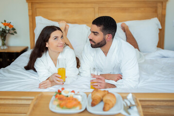 Obraz na płótnie Canvas Couple Enjoying Breakfast Lying In Bed Near Tray In Hotel