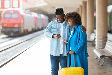 Young black couple checking time on wristwatch while standing at railway station