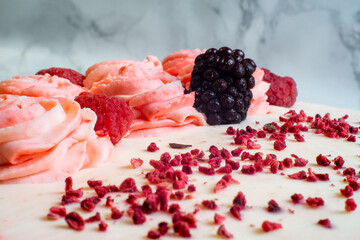 Close up macro photograph of a blackberry and raspberry cake over a dark marble backdrop
