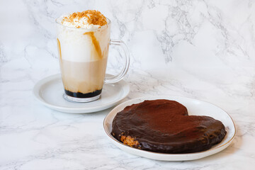 Latte macchiato specialty coffee with caramel, mocha and foam over white marble background and plate served with a chocolate butterfly cookie made of puff pastry