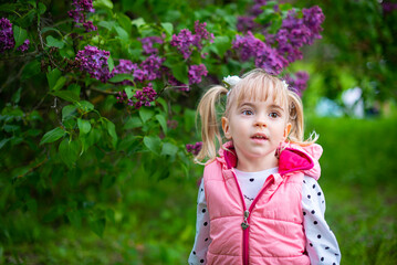 Cute little girl enjoying blooming lilac bushes in the park