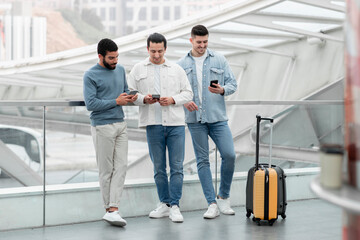 Three Males Using Cellphones Standing With Suitcase At Bus Station