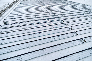 Aerial view of snow covered sustainable electric power plant with rows of solar photovoltaic panels for producing clean electrical energy. Low effectivity of renewable electricity in northern winter