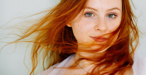 a girl with red eyes close-up in white clothes on a white background with green eyes smiles with her eyes her hair is flying