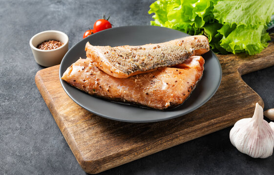 Raw salmon, greased with marinade with spices on a plate on a dark background with fresh herbs and vegetables.
