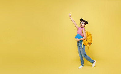 Full body smiling happy cheerful teen Asian student girl hold backpack book isolated on yellow background. Education in school concept