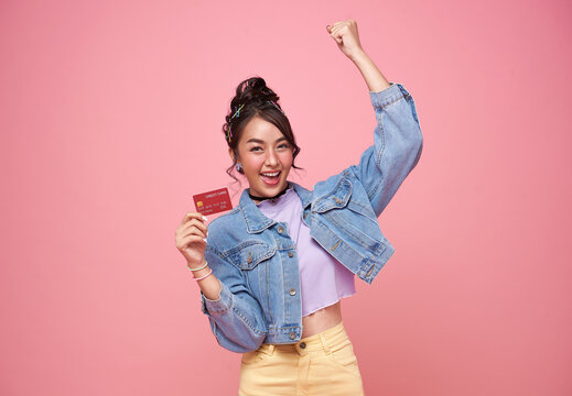 Happy young asian woman showing credit card on pink studio background. Customer girl get satisfied of credit card service with smile on face