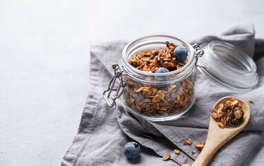 Homemade baked granola with nuts and fresh blueberry in a jar on a light background with napkin. Healthy vegetarian muesli for breakfast.