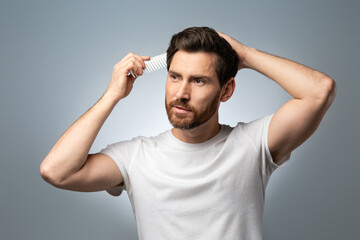 Fototapeta premium Barber shop concept. Handsome middle aged man in white t-shirt brushing his hair, standing over grey studio background