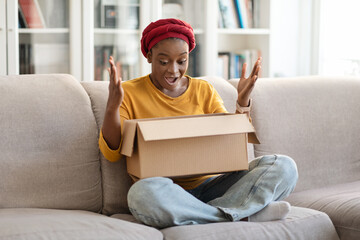 Excited african american woman looking inside paper box parcel