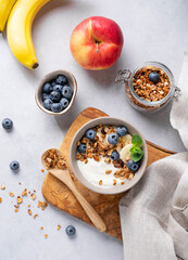 Homemade baked granola with yogurt and blueberries in a bowl on a light background with fresh...