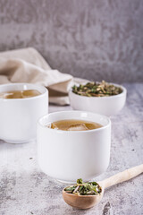 Cold green Japanese hojicha tea with ice in cups and dry tea in a bowl on the table. Vertical view