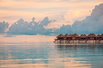 Amazing sunset panorama at Maldives. Luxury resort hotel villas seascape, calm sea water surface...