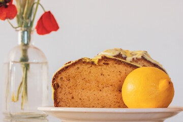 Rural still life with red poppies in glass vase and a plate with biscocho Bizcocho lemon muffin on kitchen table. Sweet dessert prepared at home. A red cup of coffee or tea. Biscotto pastries, cakes.