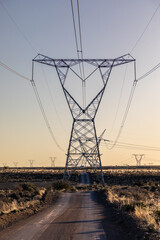 Electricity transmission pylon as dusk with a gravel access road underneath it.  