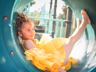 beautiful junior little girl playing in the park in yellow dress laughing with bubbles, screaming...