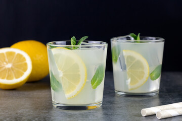 Two glasses of lemonade or a cocktail with lemon and mint on a black background. Summer refreshing drinks.