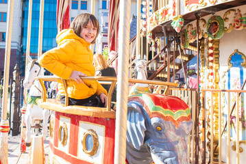 happy boy sits, rides a toy elephant on a carousel on a sunny spring day