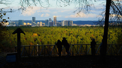 Silhouettes of people observing Vilnius city skyline from a hill in autumn