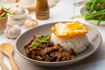 Stir fried sliced Beef with Holy Basil and Cooked Rice topped with fried egg in white plate.Thai spicy food(Pad Kra pao)