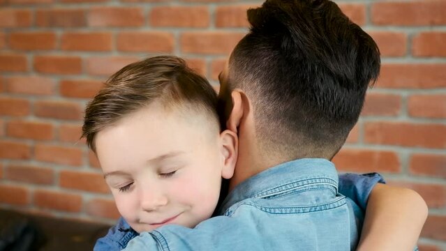 Happy Dad with son on the sofa. Happy family. Happy dad snuggles with son. Portrait of happy young family sitting on the sofa. Happy dad spending time together at home. parent kissing their child.