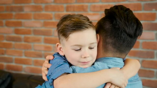 Happy Dad with son on the sofa. Happy family. Happy dad snuggles with son. Portrait of happy young family sitting on the sofa. Happy dad spending time together at home. Kids smile.