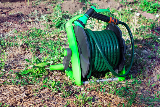 Green rubber hose reel with water spray gun. Home and gardening.