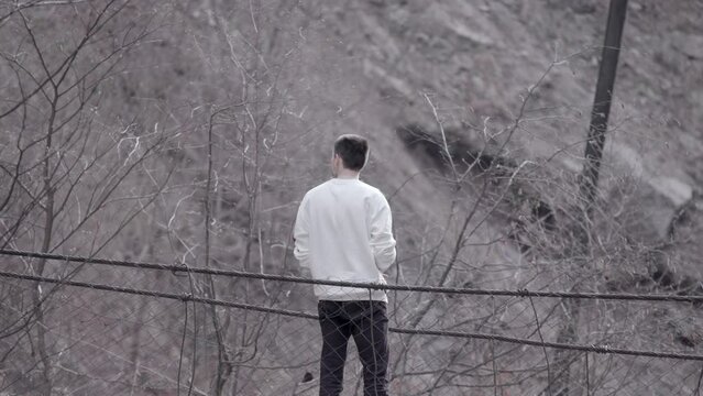 Rear view of a man standing at the edge of an autumn grey dirty slope. Stock footage. Young man looking thoughtful.