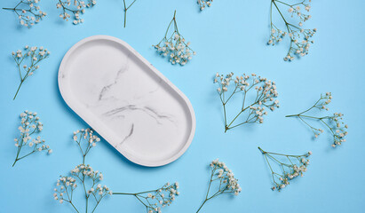 Empty oval marble decorative plate on a blue background, around a branch of gypsophila. View from above