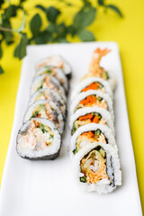 Tempura sushi roll and California roll on the white plate on yellow background. Food display and menu for restaurant and cuisine.
