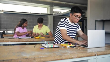 Hispanic teenager student programming digital electronics circuit in the engineering technology course