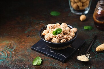 Sweets, peanuts in honey and sesame seeds in a white ceramic bowl on a pink concrete background. Useful sweets, handmade candies