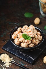 Sweets, peanuts in honey and sesame seeds in a ceramic bowl on a dark concrete background. Healthy sweets, handmade sweets.