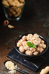 Sweets, peanuts in honey and sesame seeds in a ceramic bowl on a dark concrete background. Healthy sweets, handmade sweets.