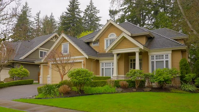 Establishing shot of two story stucco luxury house with big tree and nice landscape at spring rainfall in Vancouver, Canada, North America. Day time on April 2023. ProRes 422 HQ.