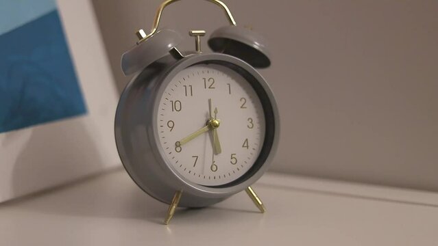 Gray alarm clock stands on a white table in the room
