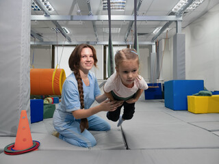 Child with physiotherapist on swing during sensory integration session. Little girl in...