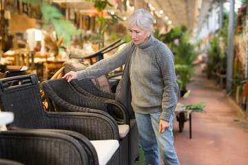 Portrait of senior woman looking for comfortable plastic rattan garden furniture in furnishings store..