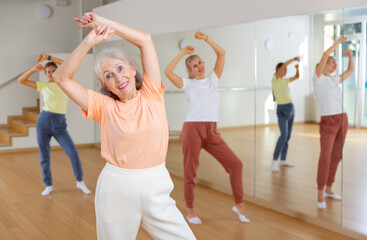 Naklejka premium Portrait of elderly smiling european woman and people dancing in modern studio