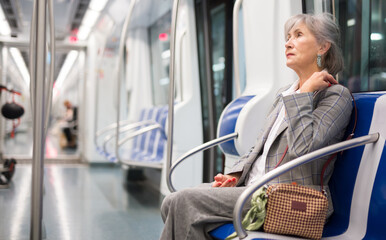 European mature woman sitting in subway train and waiting for her stop..