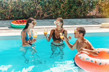 Group of friends in swimsuit drink a cocktail in a swimming pool