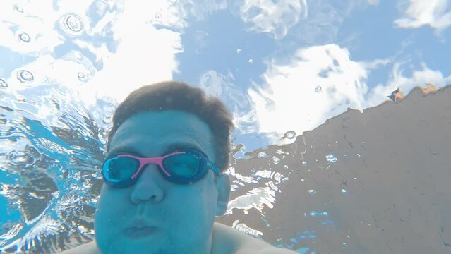a man wearing swimming goggles dives in the pool and takes a picture of himself.