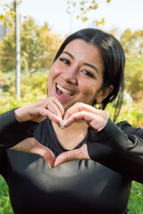 Hispanic girl making a heart with her hands in the park, big smile expressing joy