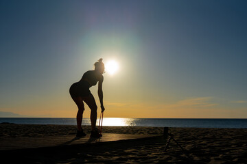 beautiful girl goes in for sports doing exercises with an expander on the seashore at dawn