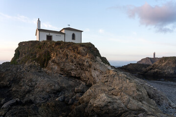Fototapeta na wymiar Virxe do Porto (Valdoviño) hermitage and Punta Frouxeira lighthouse with the cliffs in the Rias Altas touristic area of Galicia at sunset, Meiras, Spain.