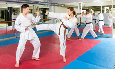 Obraz premium Teenage boy and woman in kimono sparring during group karate training. Man fighting with sparring-partner in background.