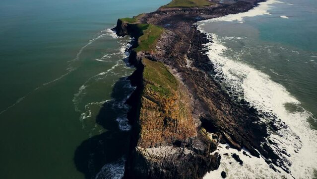 Aerial view of waves crashing onto a rocky coastline at Worm's Head on the Gower peninsula of Wales
