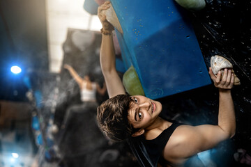 young muscular guy climbing black rock bouldering wall in gym. Sport weekend action