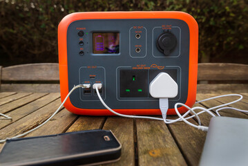 Portable power station solar electricity generator on table with mobile phone and laptop charging.