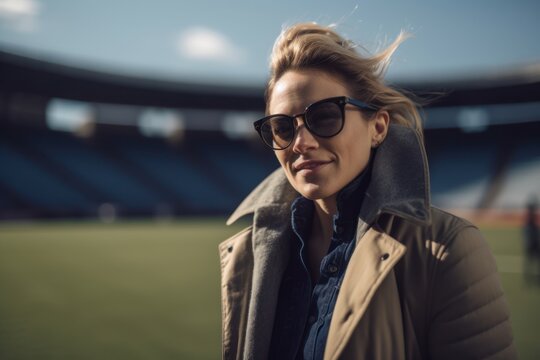 Portrait of a beautiful young woman in sunglasses and coat on the football field
